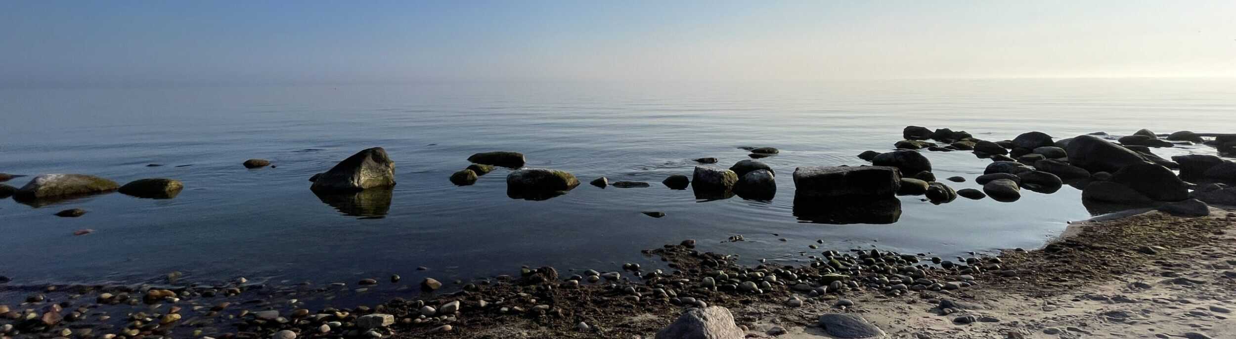 Scenic view of the Baltic Sea with smooth stones in clear water, sandy beach, and blue sky on Bornholm Island, Denmark